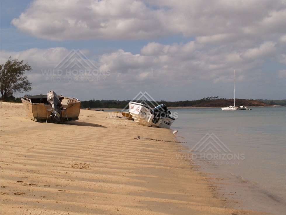 Beached dinghies on rippled sand at low tide with a shorebird. Seisia, Queensland, Australia.