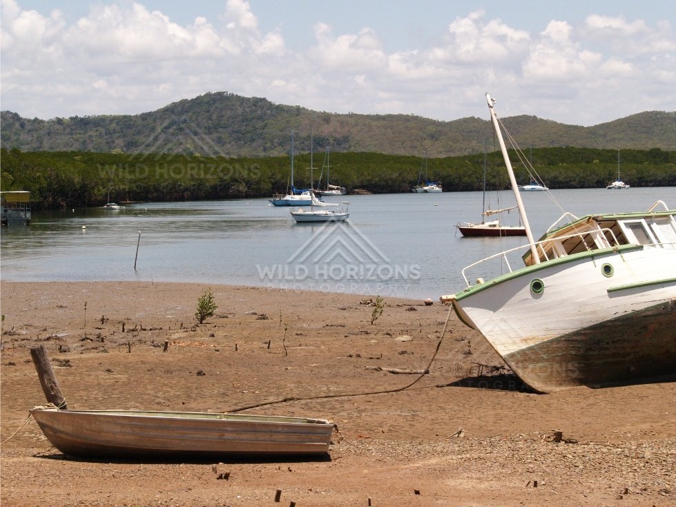 Boats and yachts in a tidal harbour with mangroves and hills. Cooktown, Australia.