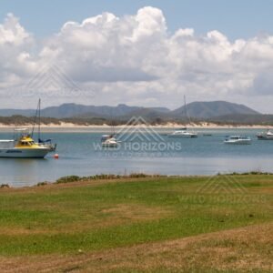 Moored boats on a calm bay with sandy shoreline and mountains beyond. Cooktown, Australia.