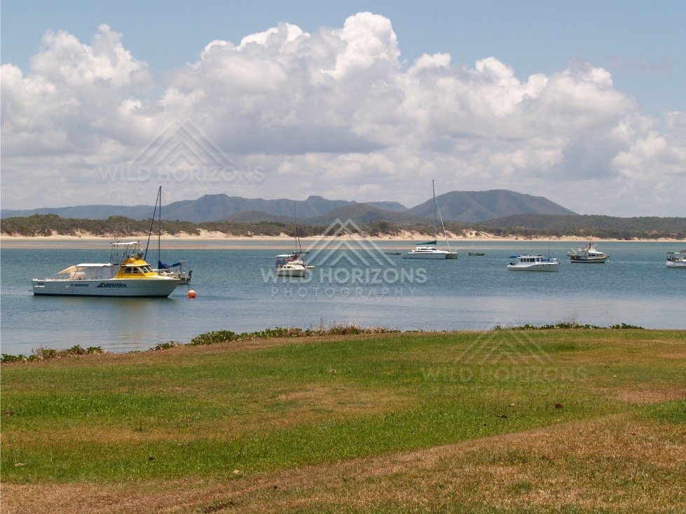 Moored boats on a calm bay with sandy shoreline and mountains beyond. Cooktown, Australia.