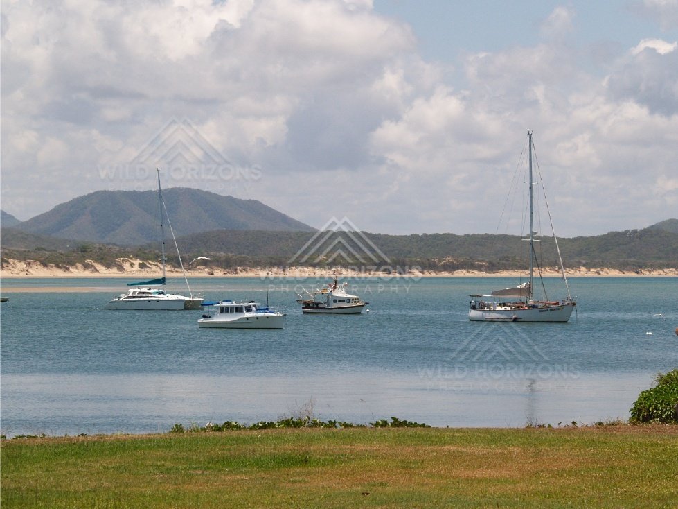 Sailing boats anchored on blue water near a sandy coast. Cooktown, Australia.
