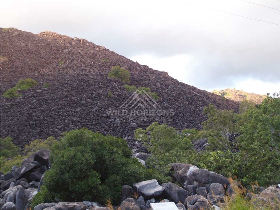 Dark boulder-strewn slope of Black Mountain rising above scrub. Black Mountain, Australia.
