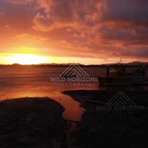 Orange sunset over a calm inlet with silhouetted masts. Cooktown, Australia.