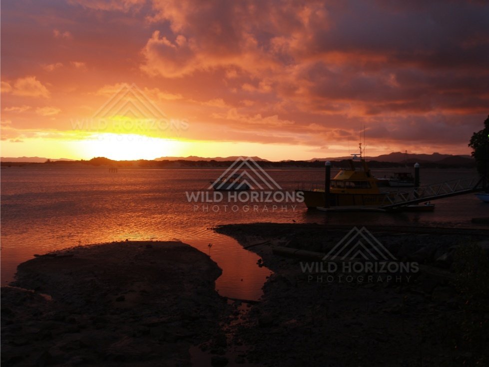 Orange sunset over a calm inlet with silhouetted masts. Cooktown, Australia.