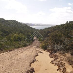 Red dirt track descending through coastal hills toward a bright bay. Elim Beach, Australia.