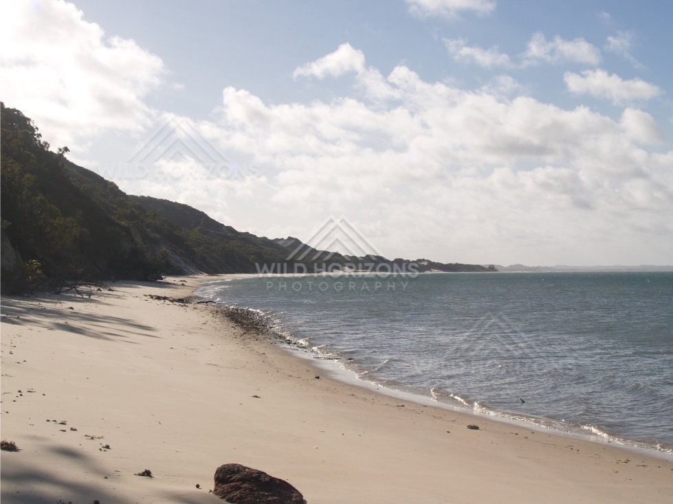 Curving tropical beach with gentle waves and scattered clouds over the sea. Elim Beach, Australia.