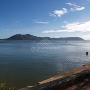 Calm harbour water with a distant headland beneath a bright blue sky. Cooktown, Australia.