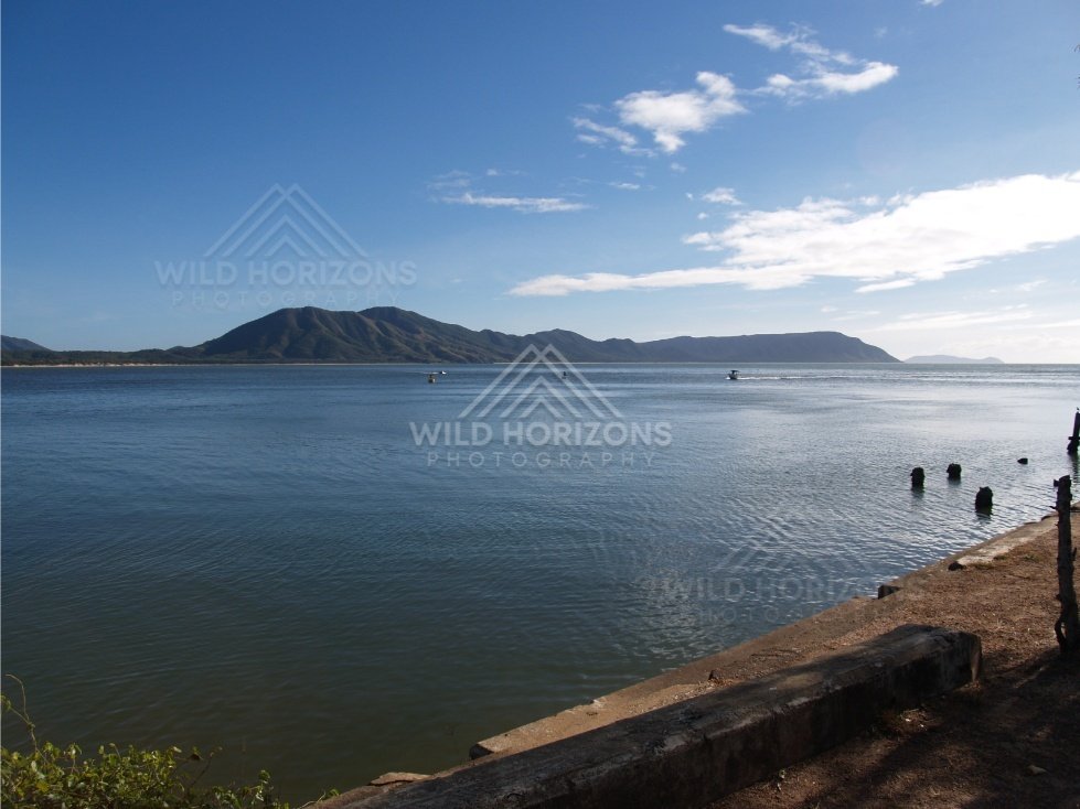 Calm harbour water with a distant headland beneath a bright blue sky. Cooktown, Australia.
