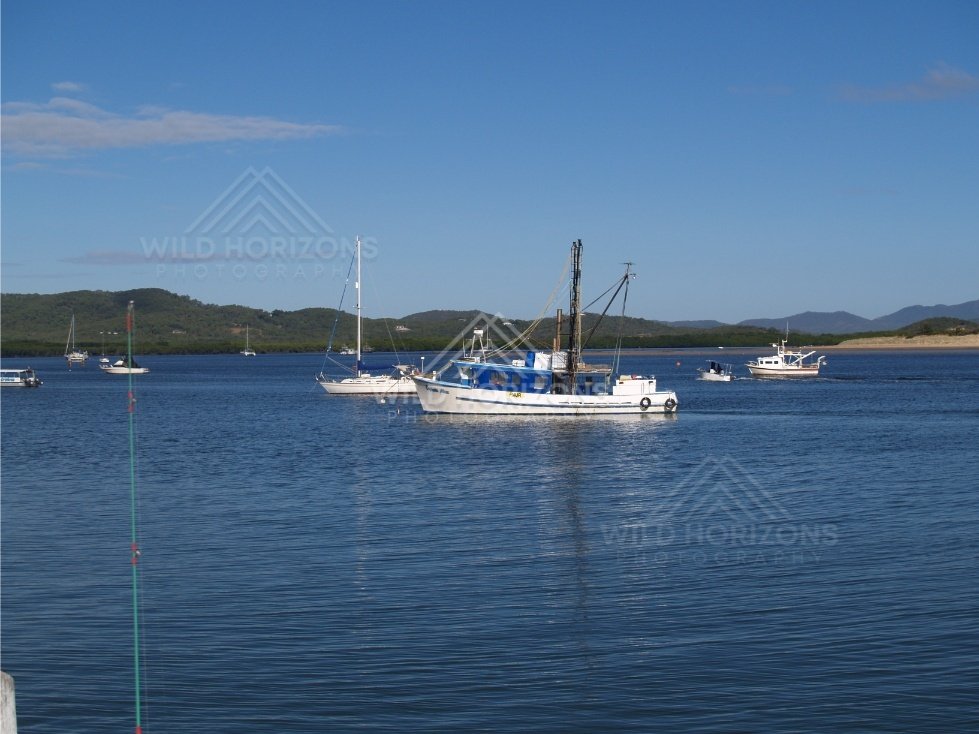 Moored yachts on blue harbour water with green hills beyond. Cooktown, Australia.