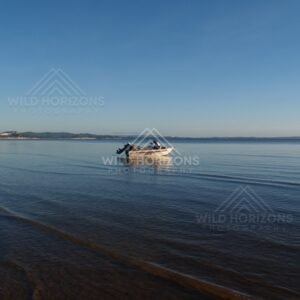 Small boat anchored on calm water with sandbars and distant coastline. Elim Beach, Australia.