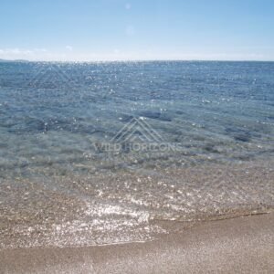 Sunlit ripples across clear shallow sea with a low island on the horizon. Elim Beach, Australia.
