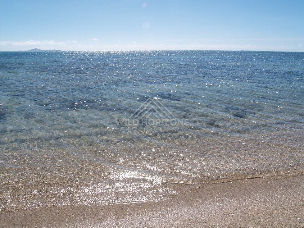 Sunlit ripples across clear shallow sea with a low island on the horizon. Elim Beach, Australia.