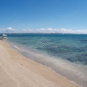 Curving beach with a small boat anchored near the shoreline in turquoise water. Elim Beach, Australia.