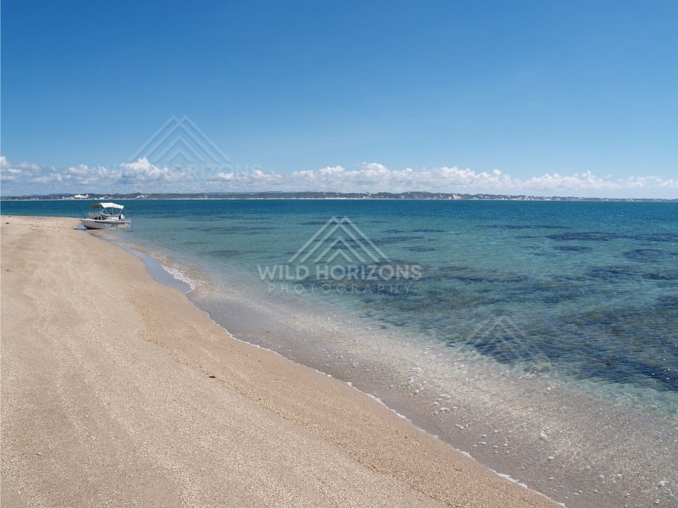 Curving beach with a small boat anchored near the shoreline in turquoise water. Elim Beach, Australia.