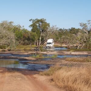 4WD vehicle positioned at a shallow creek crossing on a dirt track with water channels and grass. Lakefield National Park, Australia.