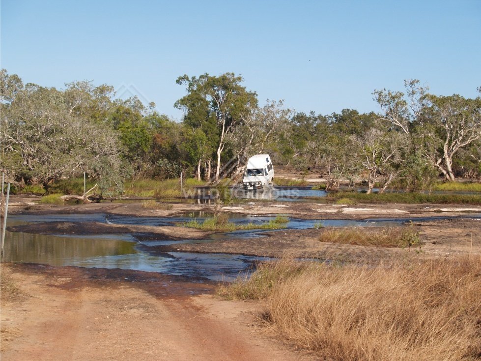 4WD vehicle positioned at a shallow creek crossing on a dirt track with water channels and grass. Lakefield National Park, Australia.