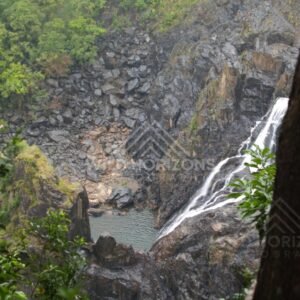 Waterfall dropping through dark rock into a narrow rainforest gorge. Kuranda, Australia.