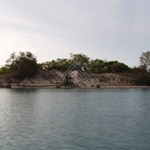 Sandy riverbank with shrubs and trees beside calm water. Jardine River, Queensland, Australia.