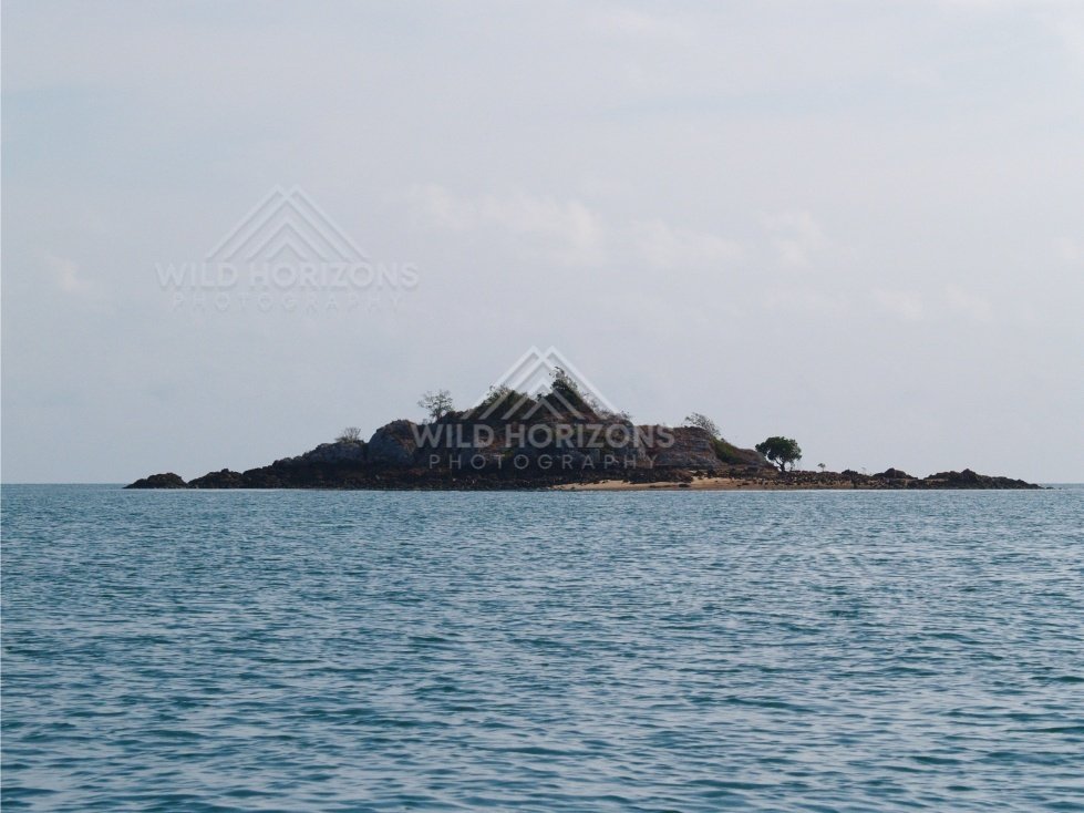 Rocky islet with scattered trees in open sea. Cape York, Queensland, Australia.