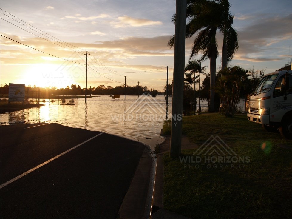 Flooded Bundaberg street at sunset with parked vehicles. Bundaberg, Australia.
