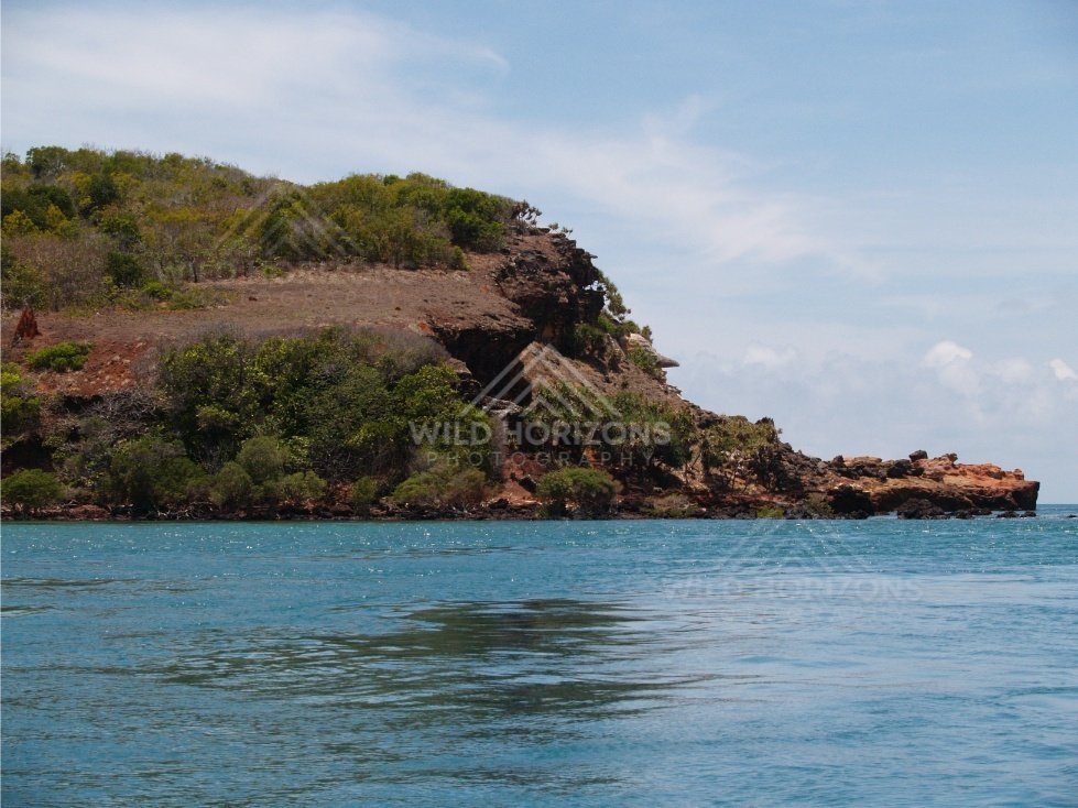 Close coastal headland with exposed red rock and vegetation. Cape York, Queensland, Australia.