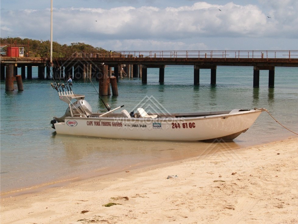 Aluminium boat on sand in front of a timber wharf. Seisia, Queensland, Australia.