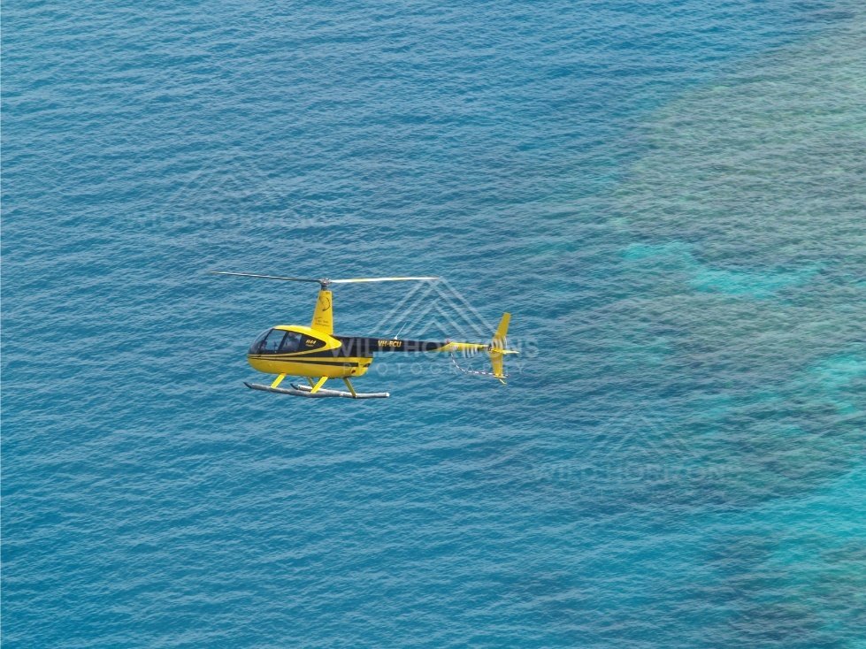 Yellow helicopter flying over turquoise reef waters. Thursday Island, Queensland, Australia.